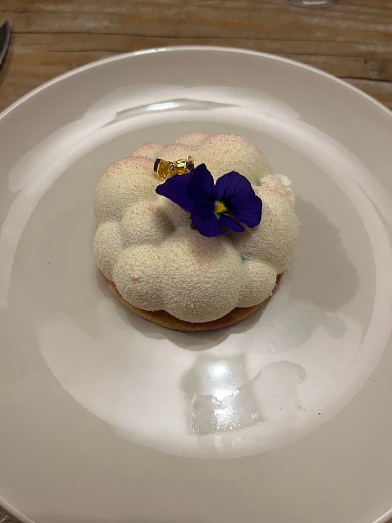 Dessert blanc en forme de nuage sur un fond de tarte, avec une feuille d’or et une pensée violette